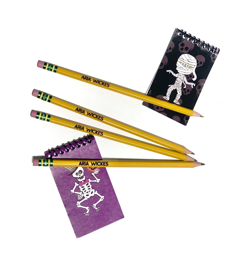 Set of four yellow personalized pencils with black printed name paired with small Halloween-themed notepads on white background