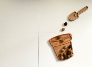 Wooden garden spade sensory tray with felt balls and a small matching shovel on white surface
