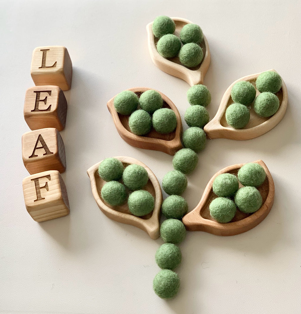 Small wooden leaf-shaped trays with green felt balls and wooden letter blocks spelling leaf on white surface