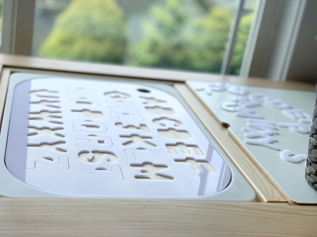 Uppercase alphabet puzzle tabletop insert with white acrylic letters and maple plywood base in wooden frame near window light