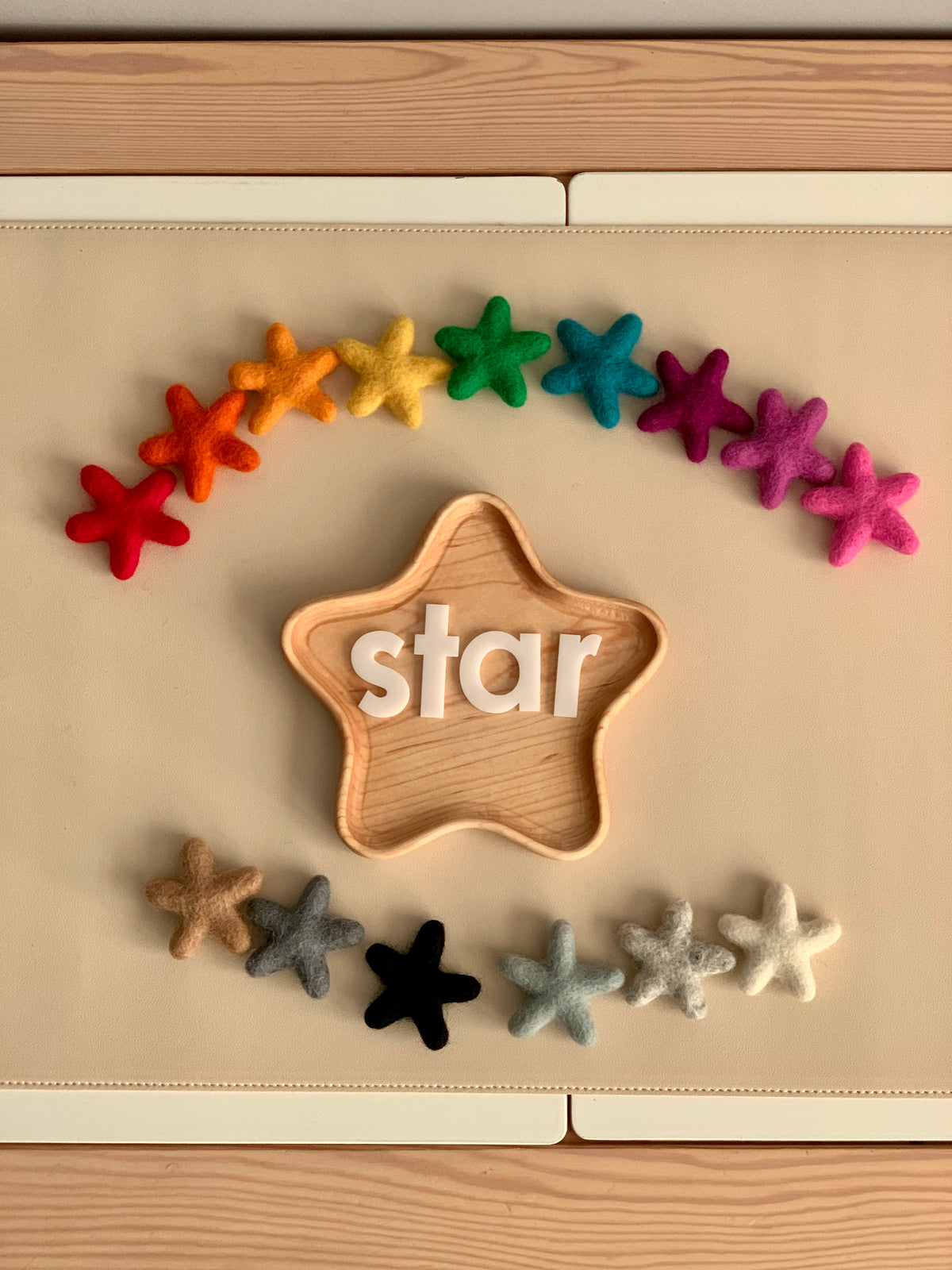 Handmade wool felt stars in various colors arranged around a wooden star-shaped tray with white letter blocks spelling star