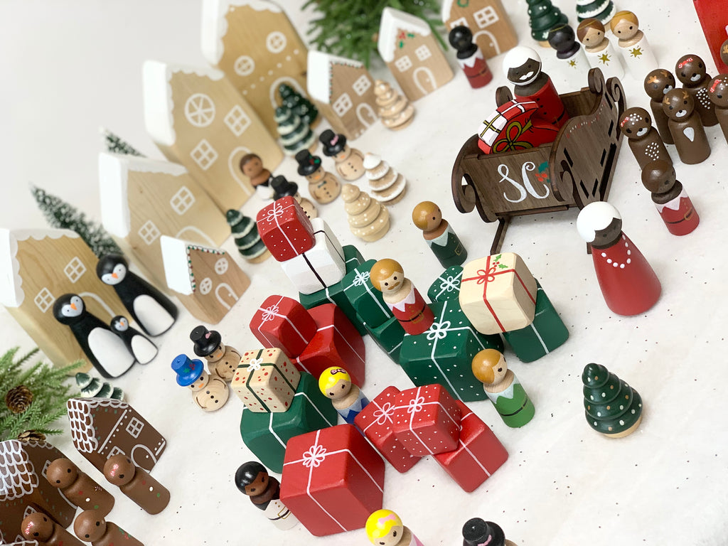 Hand-painted Christmas peg dolls with Santa, reindeer, gingerbread, presents, trees, and snowy village background