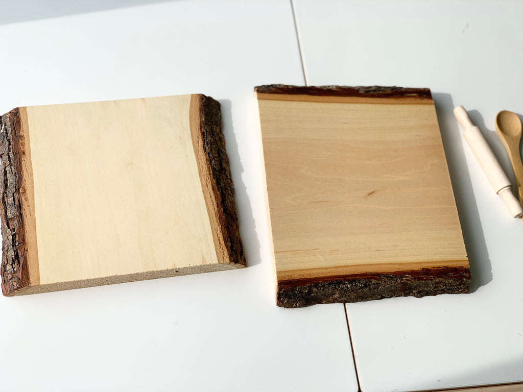 Two clear-coated live edge wooden trays with natural bark edges on white surface with wooden utensils nearby