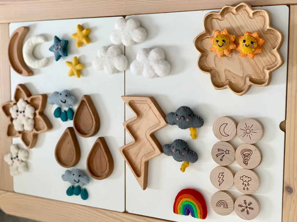 Wooden weather memory game with hand-drawn icons, clouds, raindrops, lightning, and colorful felt weather shapes on white board