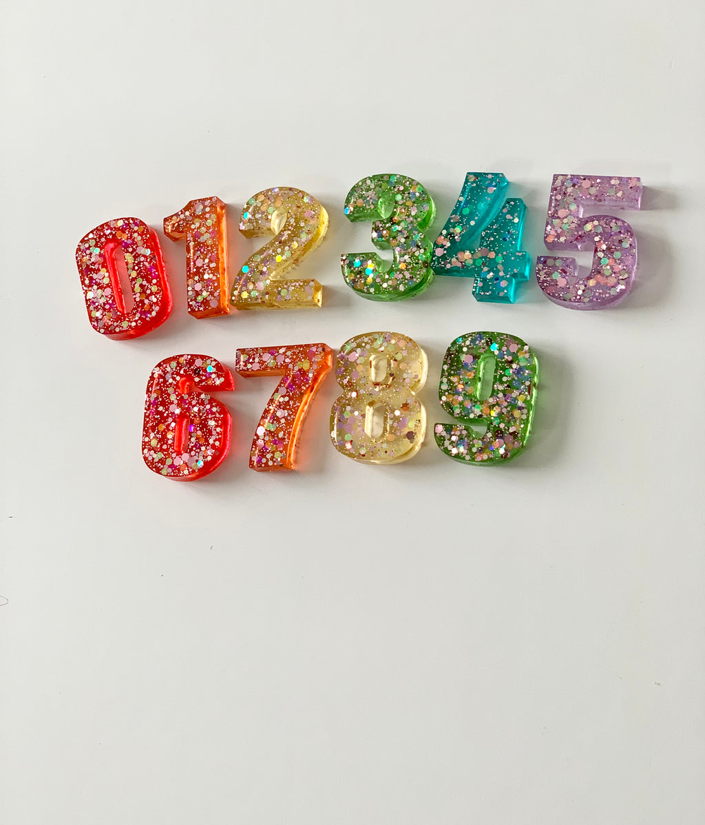 Rainbow glitter resin numbers 0 to 9 arranged on white background with multicolored sparkles inside