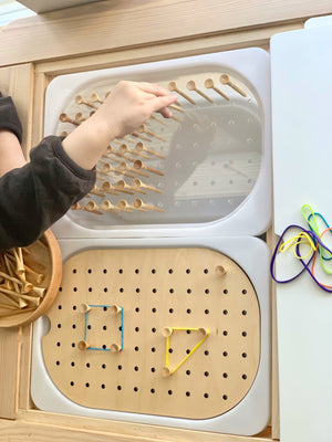 Child’s hand placing wooden golf tees into a Flisat peg board insert with elastic bands and wooden bowl on light wood surface