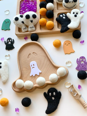Ghost-shaped wooden sensory tray with felt balls and assorted felt ghost decorations on white background
