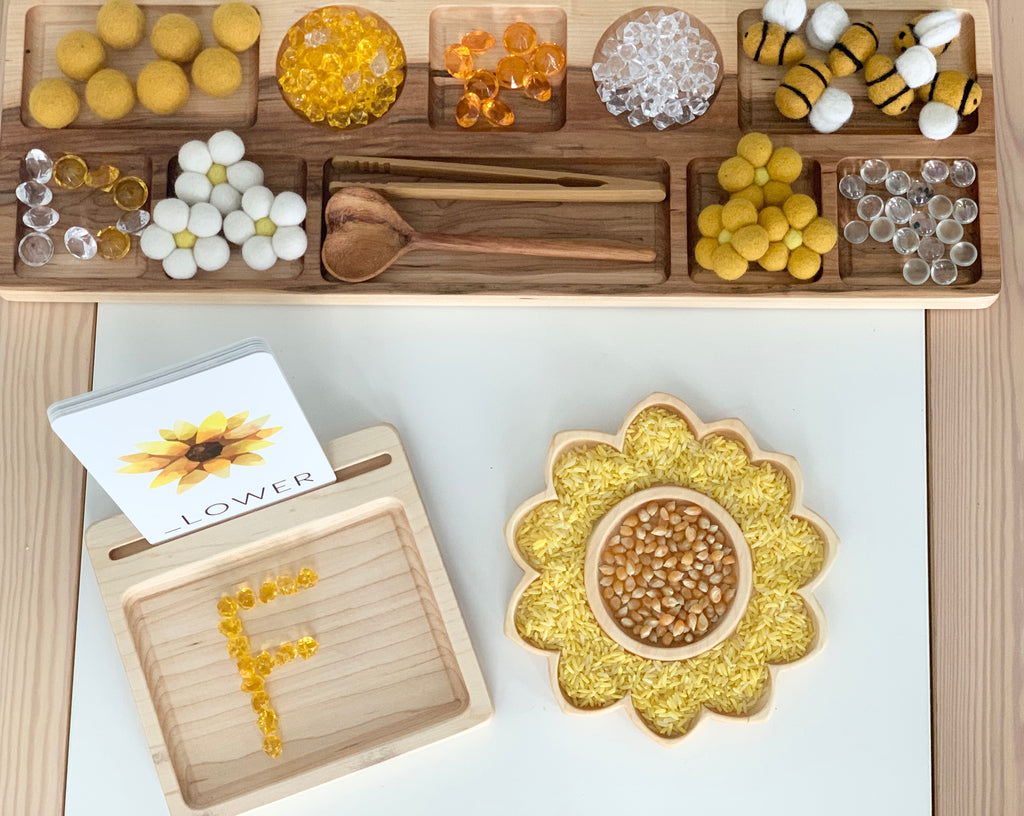 Wooden sensory tray set with sunflower-shaped plate filled with yellow rice and popcorn kernels on light wood surface