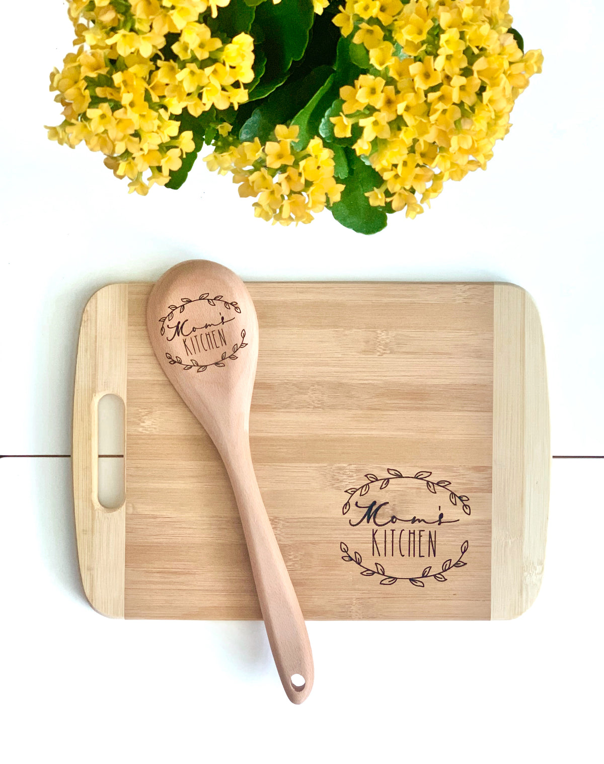 Personalized bamboo cutting board and wooden spoon set engraved with Mom’s Kitchen text and decorative leaf design