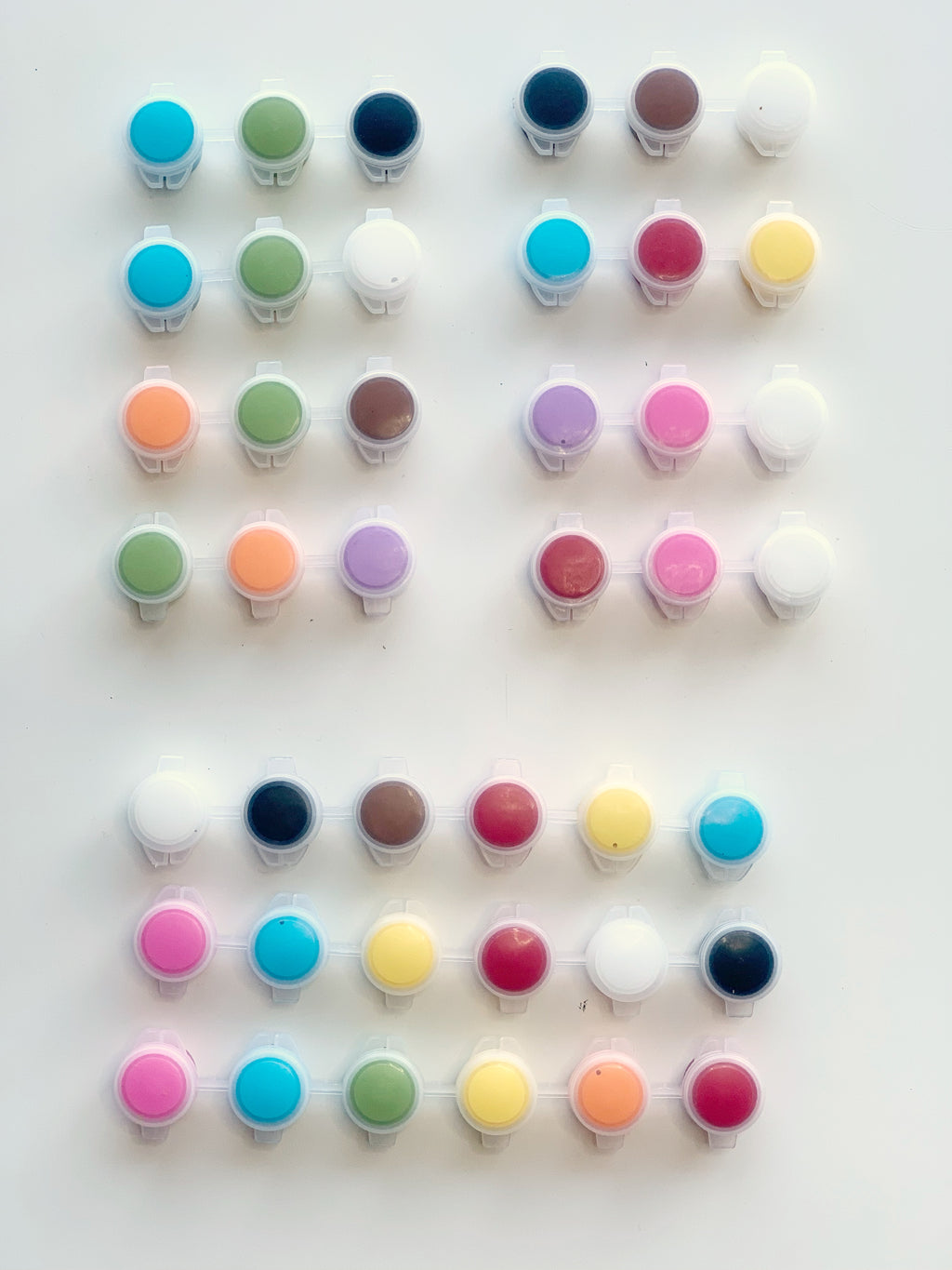 Small paint pots in various colors arranged in rows on white background for DIY craft projects