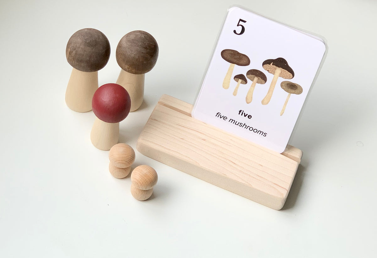 Natural wooden flash card holder with mushroom-themed flash card and wooden mushroom figurines on white background