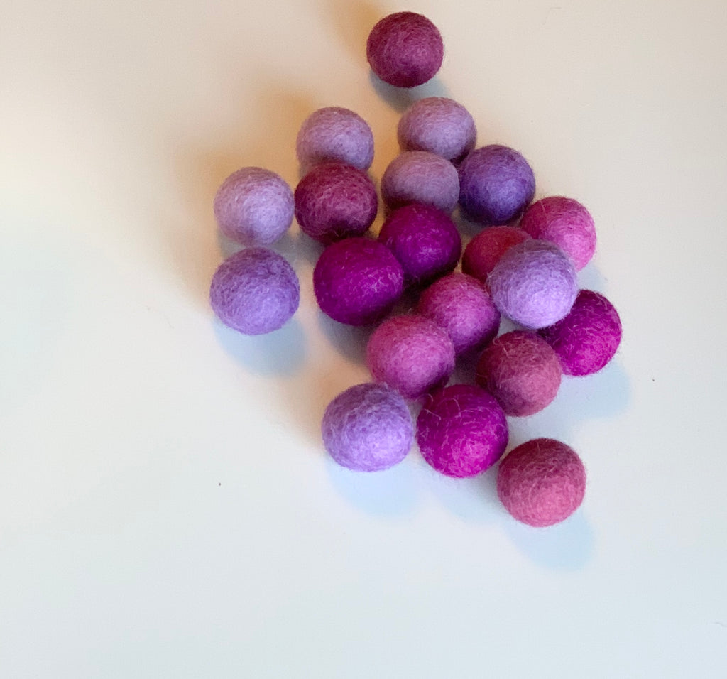 Assorted purple felt balls in varying shades scattered on a white surface in soft natural light
