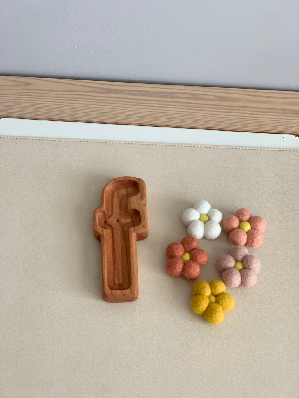 Natural wooden lowercase letter f sensory tray next to small colorful felt flower shapes on beige surface