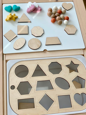 Wooden shape sorter insert with various geometric shapes and felt balls on white acrylic Flisat table top