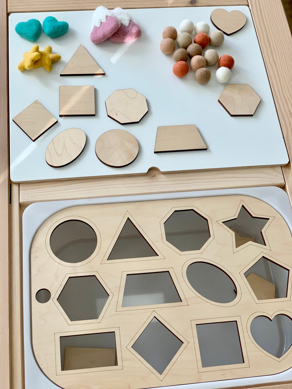 Wooden shape sorter insert with various geometric shapes and felt balls on white acrylic Flisat table top