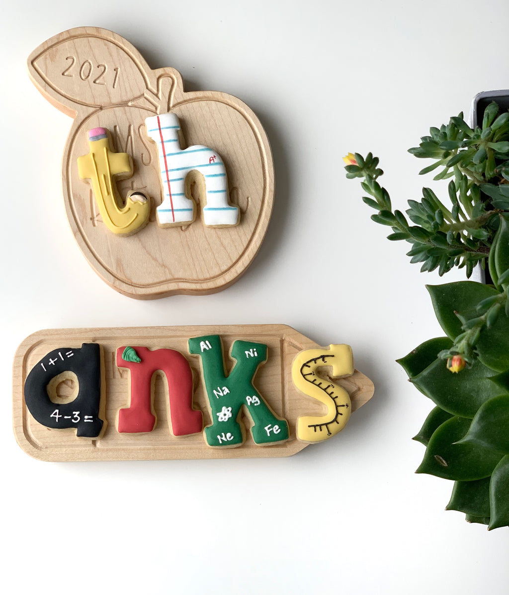 Personalized wooden teacher name plate with colorful letters and educational designs on apple and rectangular plaques with plants nearby