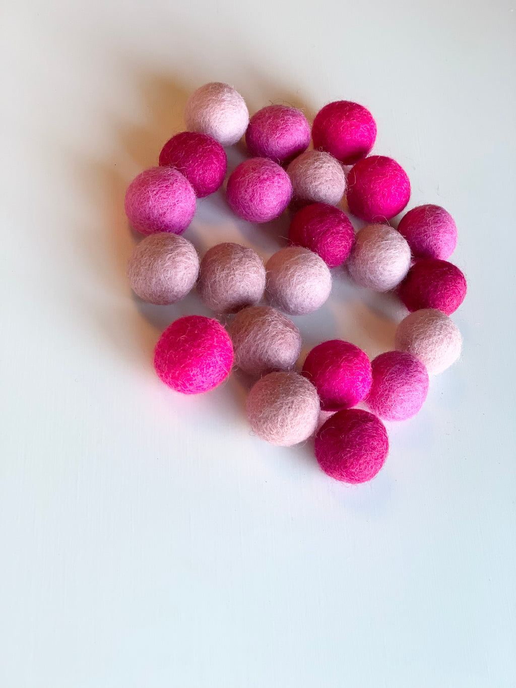 Assorted pink felt balls in varying shades arranged on a white surface with soft natural lighting
