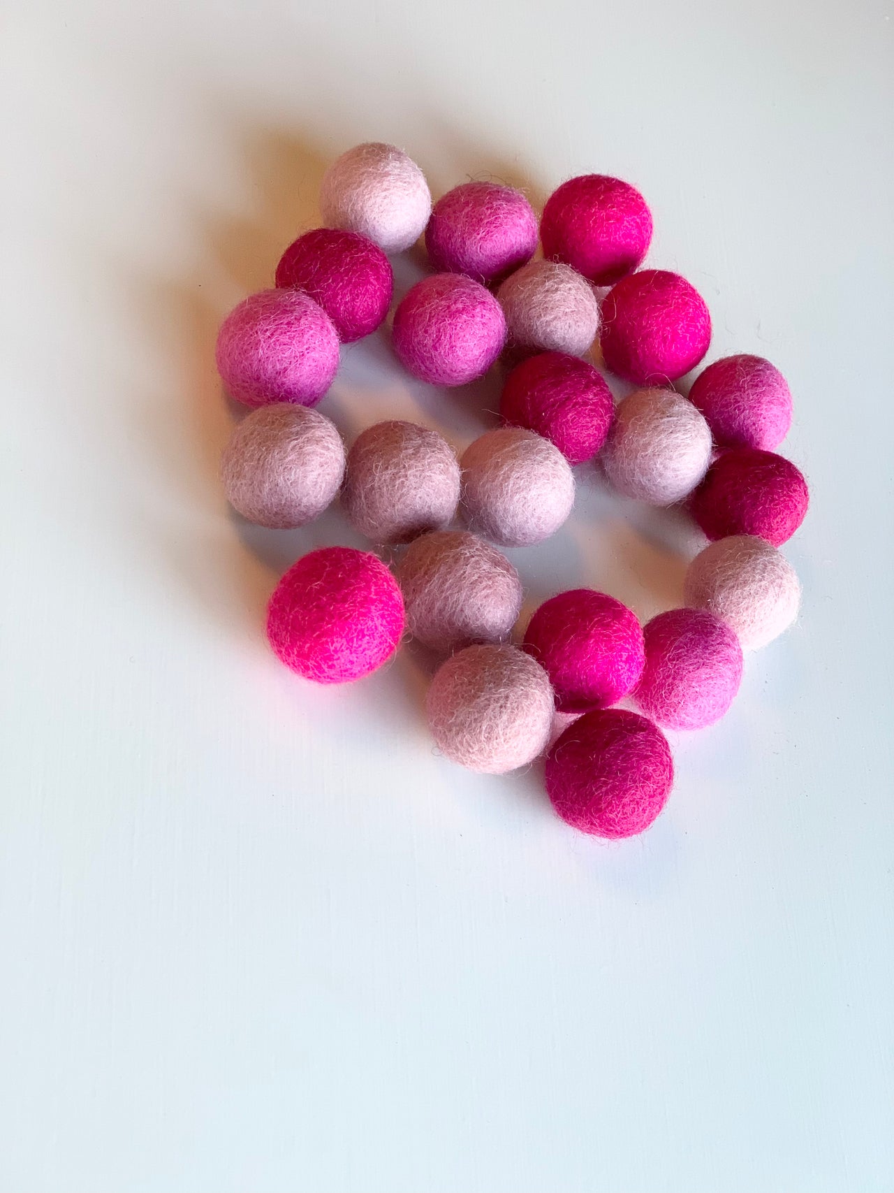 Assorted pink felt balls in varying shades arranged on a white surface with soft natural lighting