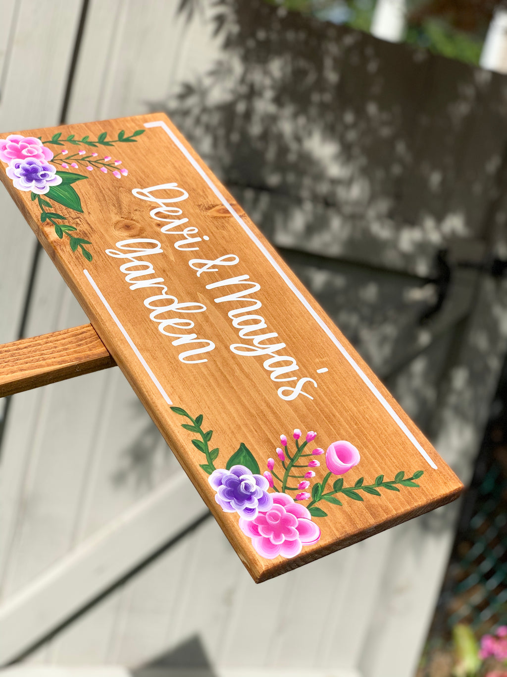 Large custom wooden garden sign with white cursive letters and pink and purple floral accents on natural wood grain background