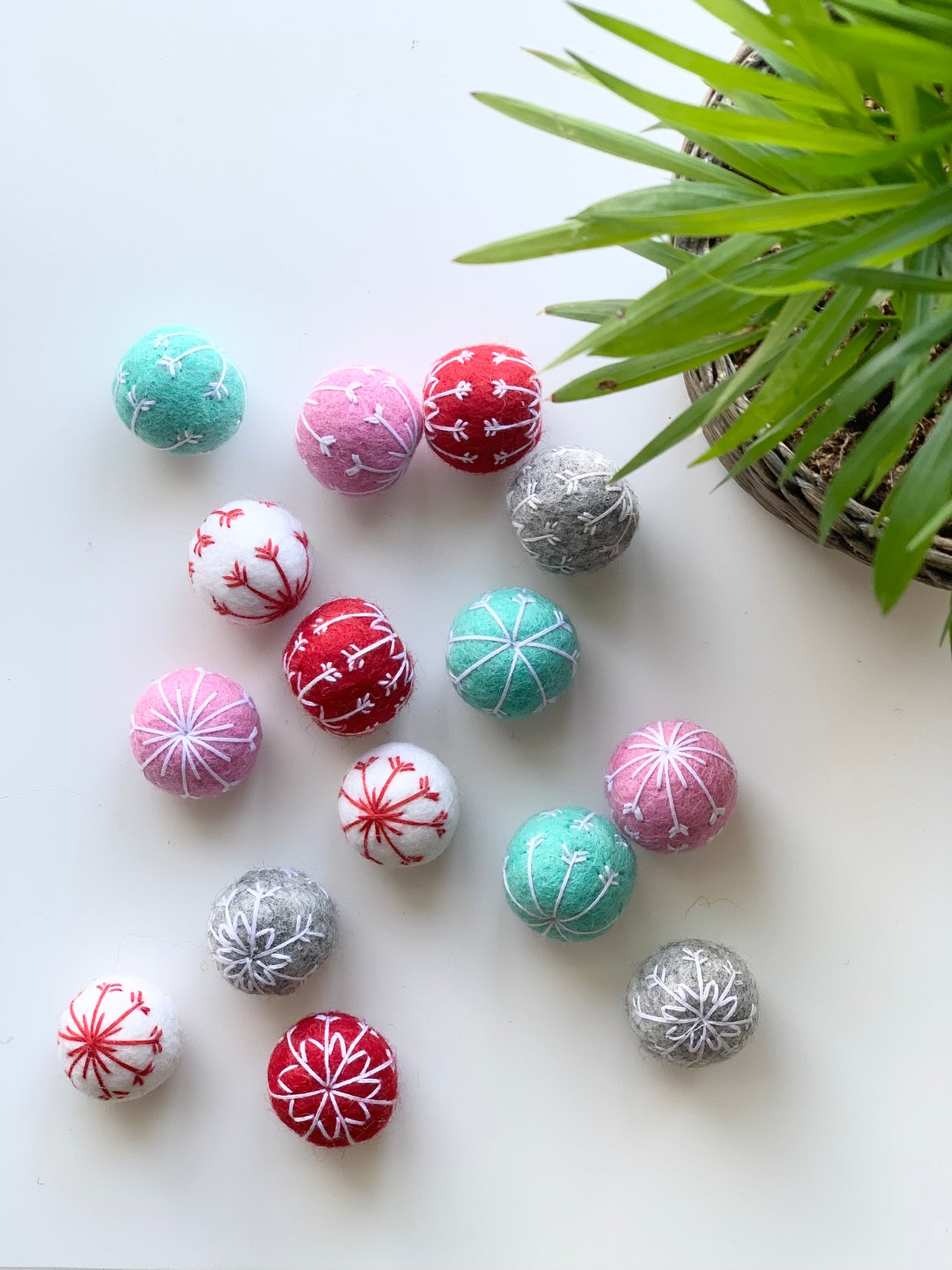 Assorted handmade felt snowflake balls in red, pink, white, turquoise, and gray with embroidered designs on white background