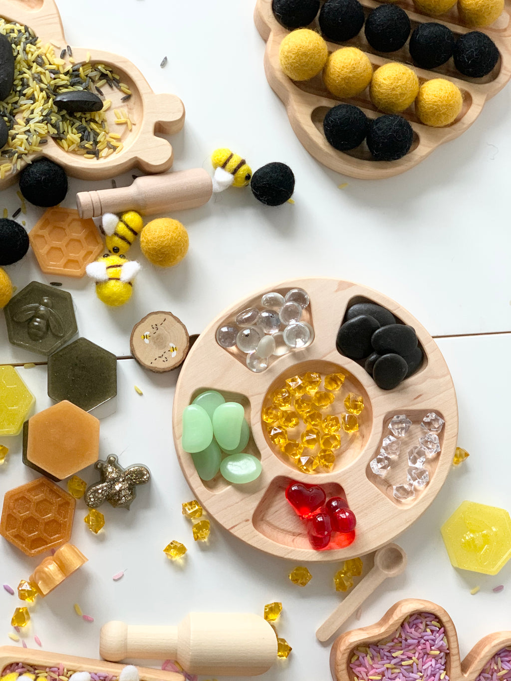 Round wooden Tinker Tray with six compartments holding colorful sensory play items on white background