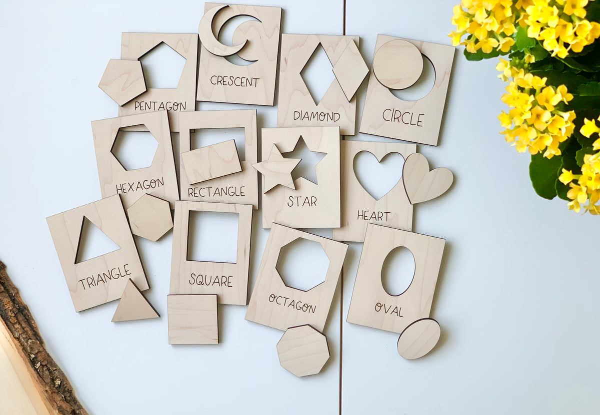 Natural wooden shape puzzle flash cards with cutouts and shape names arranged on white surface near yellow flowers