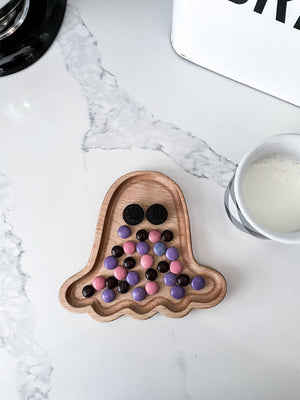Small natural wood ghost-shaped sensory tray with colorful candy and black cookie eyes on white marble surface