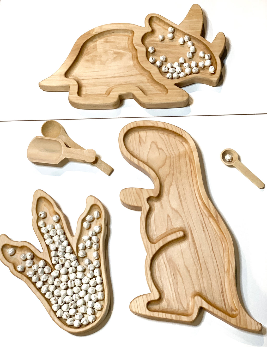 Natural wooden T-Rex shaped sensory tray with scoops and dinosaur footprint tray filled with white beads on white background