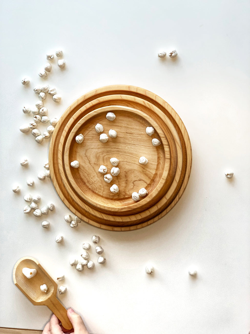 Three nested round natural wooden plates with small white beans scattered inside and around on white surface