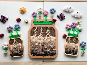 Large wooden sensory tray shaped like a jar with soil layers, roots, rocks, and colorful felt flowers on white background