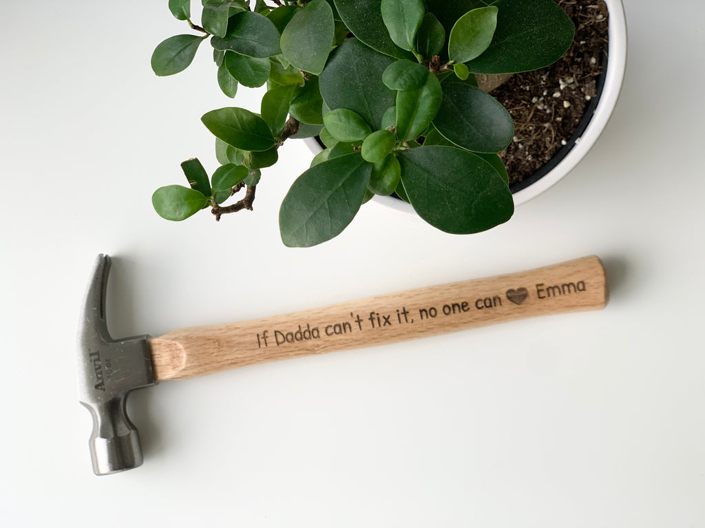 Personalized wooden hammer with laser engraved custom message and heart icon on natural wood handle near green potted plant
