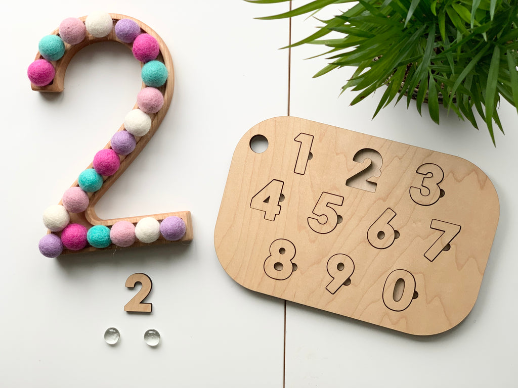 Maple plywood number puzzle tabletop insert with engraved numbers 0-9 on white surface with wooden number and felt balls nearby