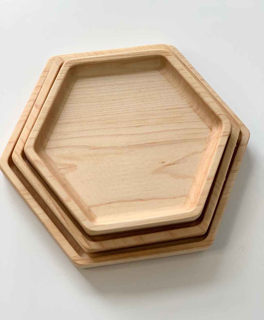 Set of three natural wooden nesting hexagon plates stacked on white surface with smooth finish