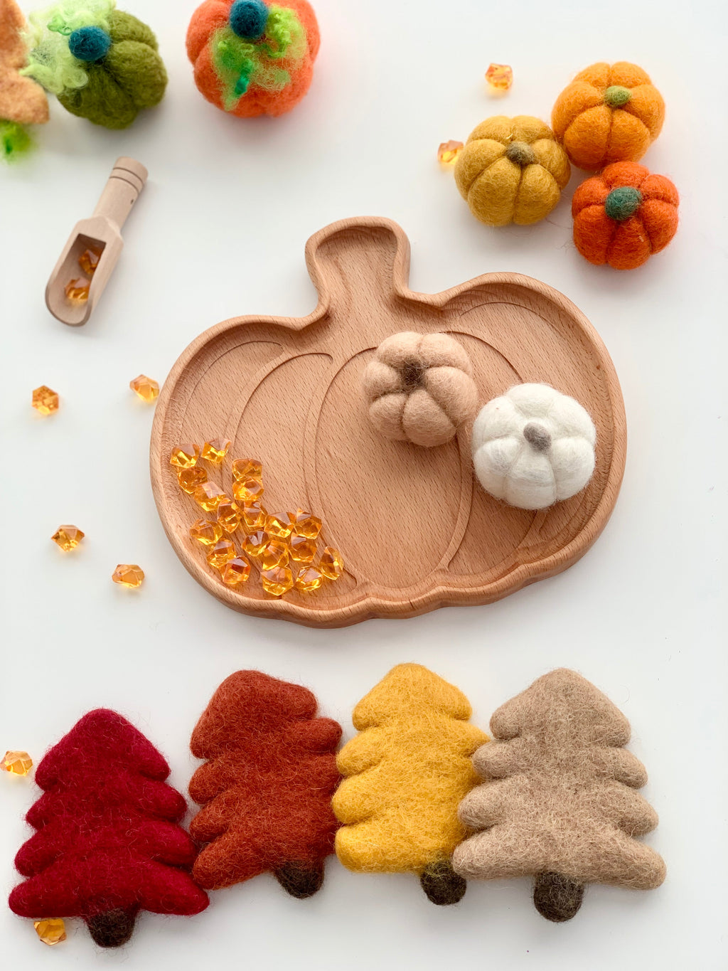 Small natural wooden pumpkin-shaped sensory tray with felt pumpkins and colorful felt pine trees on white surface