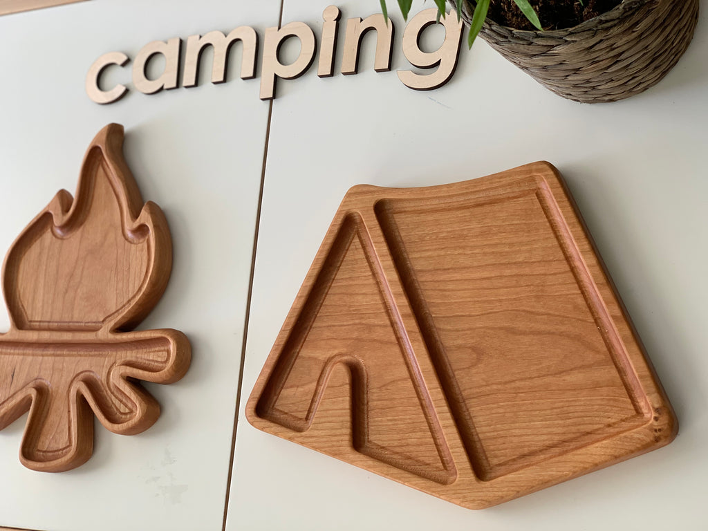 Natural wooden sensory tray shaped like a tent with a campfire-shaped compartment on white surface and "camping" letters above