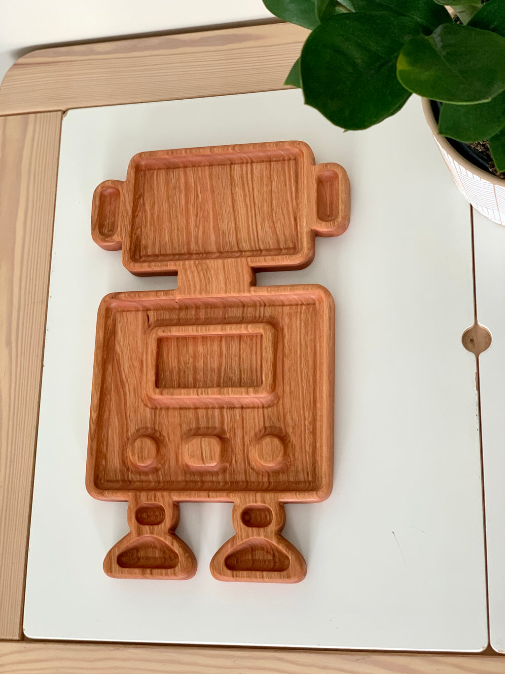 Wooden robot-shaped sensory tray with multiple compartments on white table next to green plant