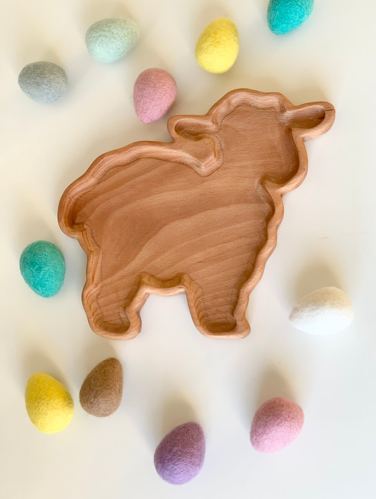 Wooden lamb-shaped sensory tray surrounded by pastel felt eggs on white surface for spring activities