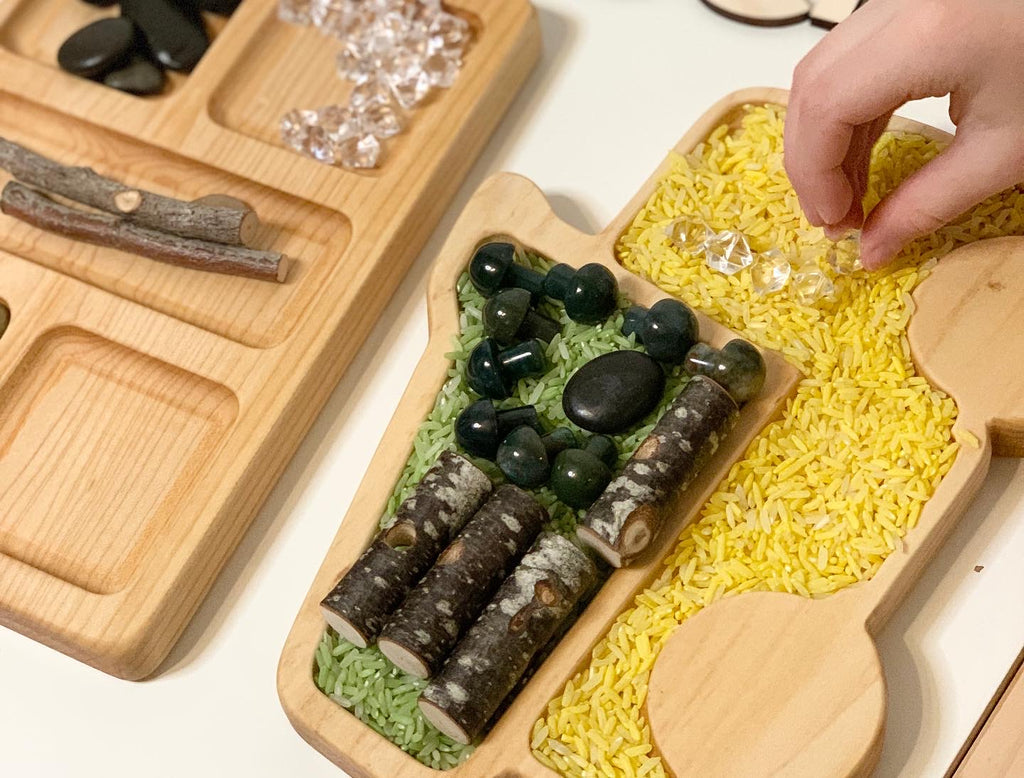 Wooden dump truck sensory tray filled with colored rice, wooden beads, stones, and child's hand arranging clear beads