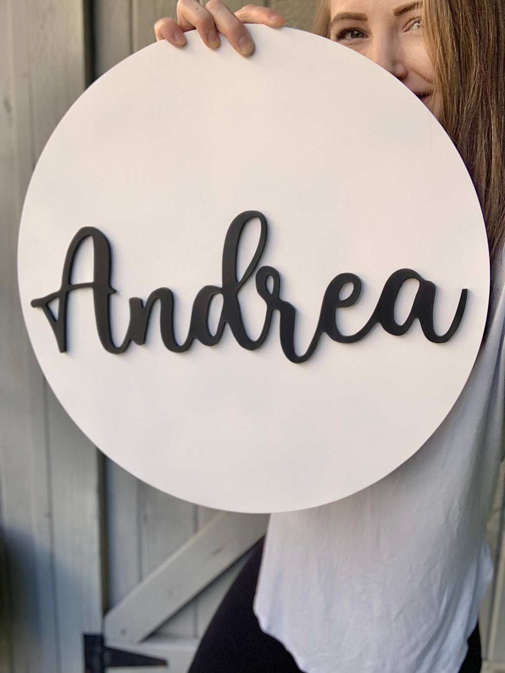 3D round white wooden name sign with black cursive letters spelling Andrea held by woman