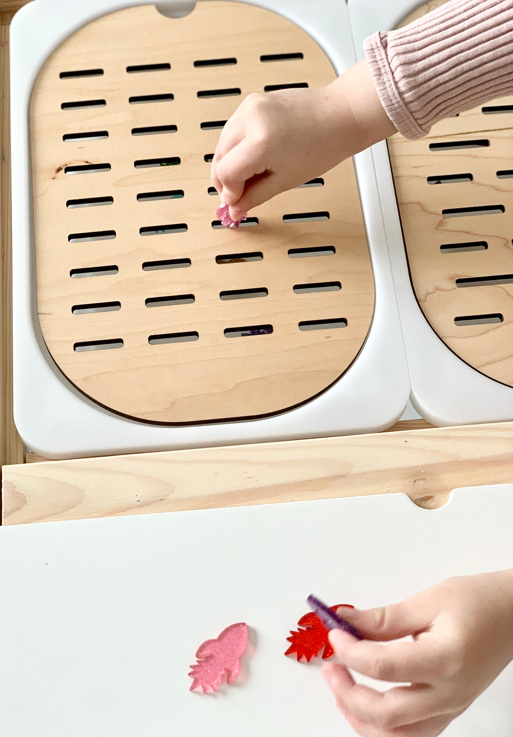 Child placing colorful acrylic shapes into wooden Slots Sorter Flisat Table Top Insert with small slots on white table