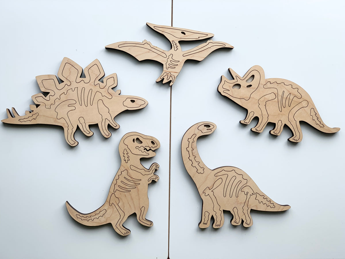 Set of five natural wooden dinosaur skeleton puzzles with engraved bone details on plain background