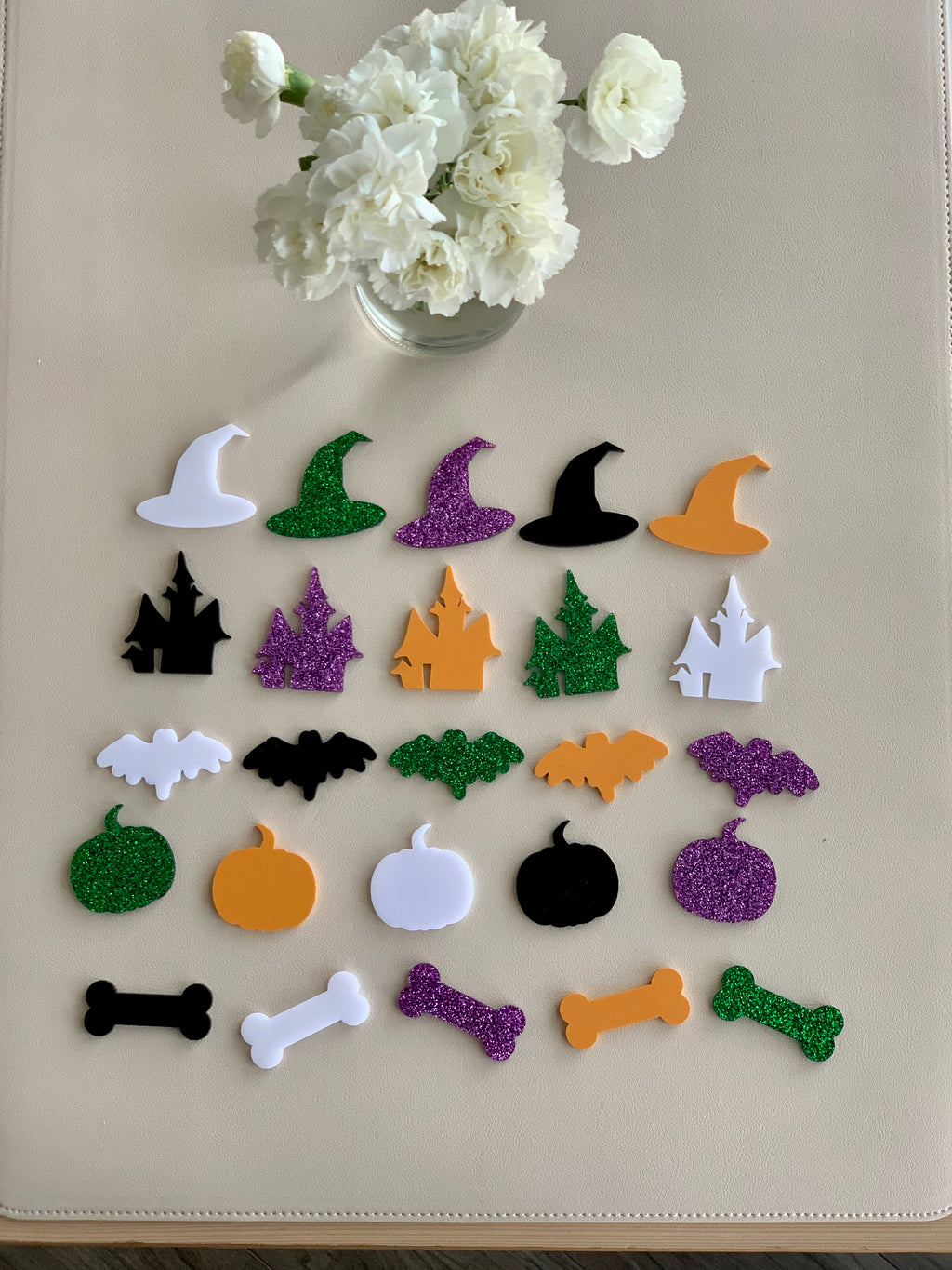 Assorted Halloween acrylic shapes including witches hats, haunted houses, bats, pumpkins, and bones in various colors on beige surface