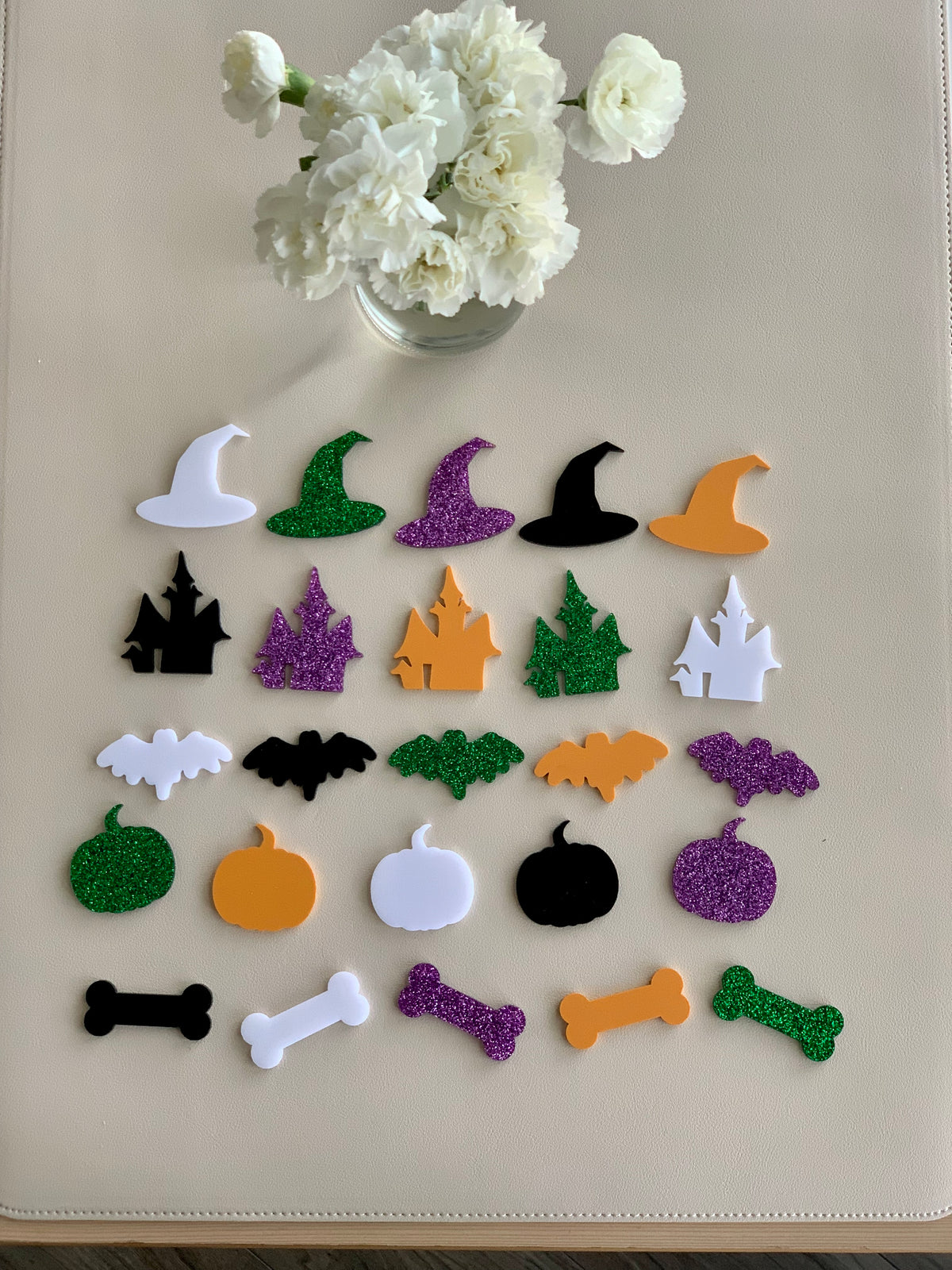Assorted Halloween acrylic shapes including witches hats, haunted houses, bats, pumpkins, and bones in various colors on beige surface