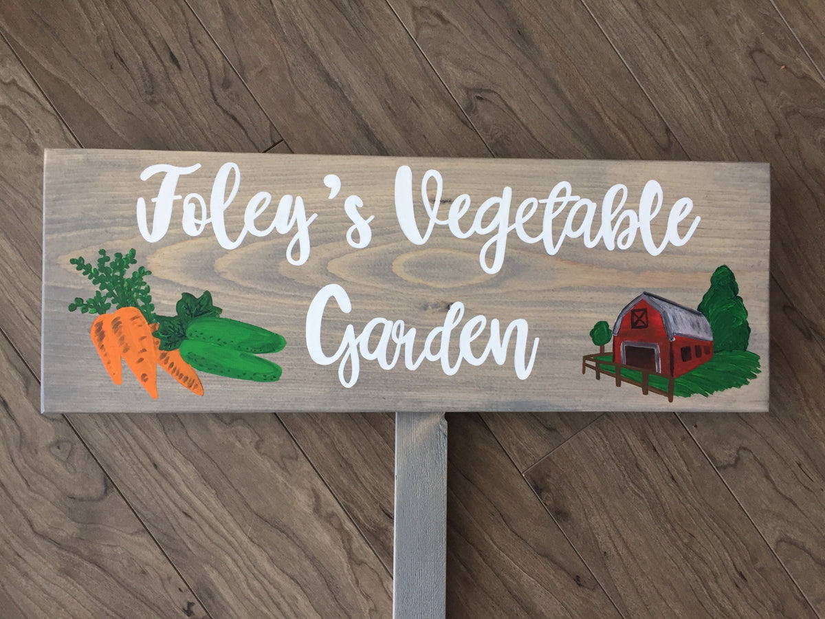 Large custom wooden vegetable garden sign with white cursive letters and carrot, cucumber, and red barn illustrations on wood background