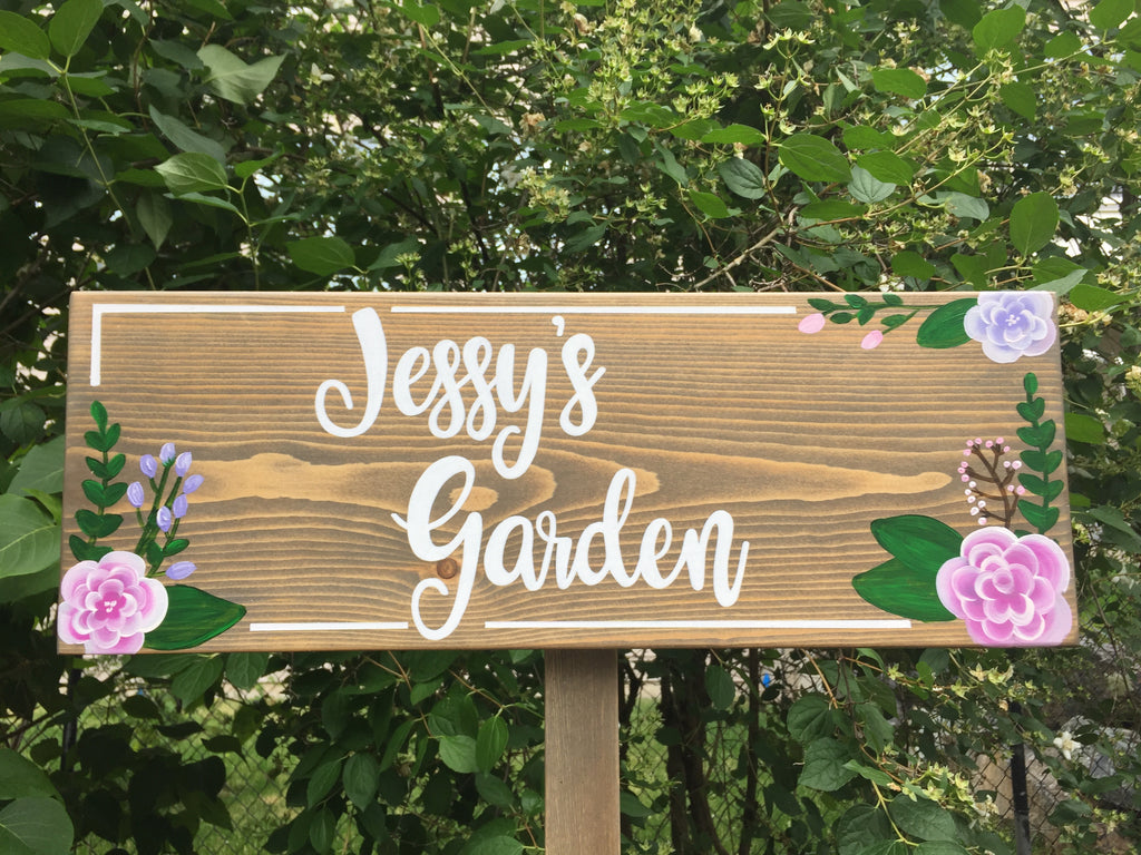 Large personalized wooden garden sign with white cursive letters and pink and purple floral accents on natural wood background