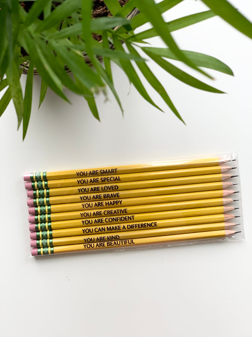 Set of yellow personalized pencils with positive affirmations printed in black and pink erasers in clear packaging on white surface