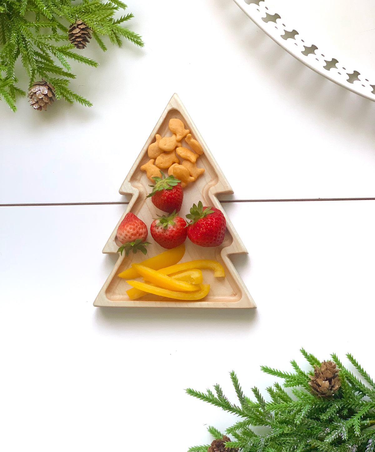 Natural wooden tree-shaped sensory tray holding strawberries, yellow bell pepper slices, and goldfish crackers on white surface