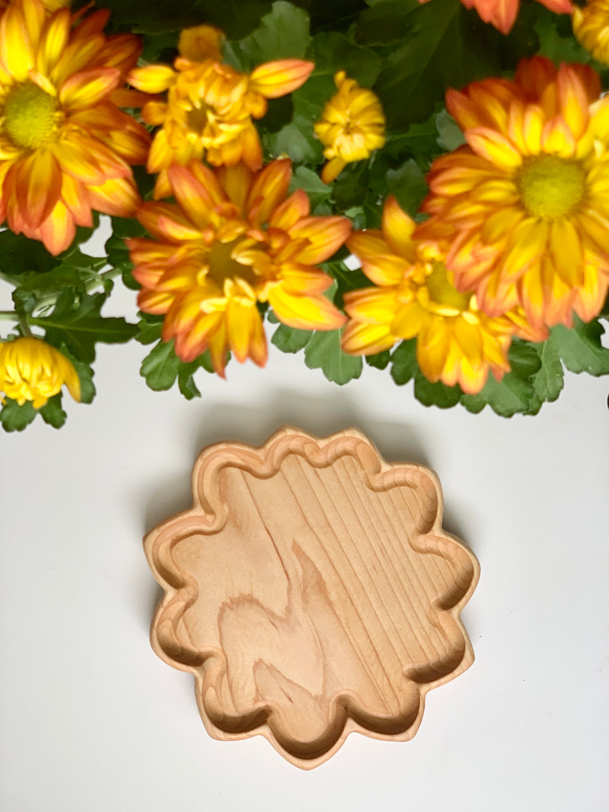 Small natural wooden flower-shaped sensory tray on white surface with yellow and orange flowers above