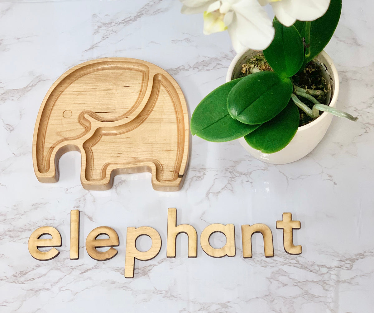 Elephant-shaped wooden sensory tray with carved details next to wooden letters spelling elephant on marble surface