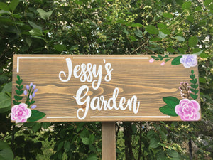 Large custom wooden garden sign with white cursive letters and pink and purple floral illustrations on natural wood background